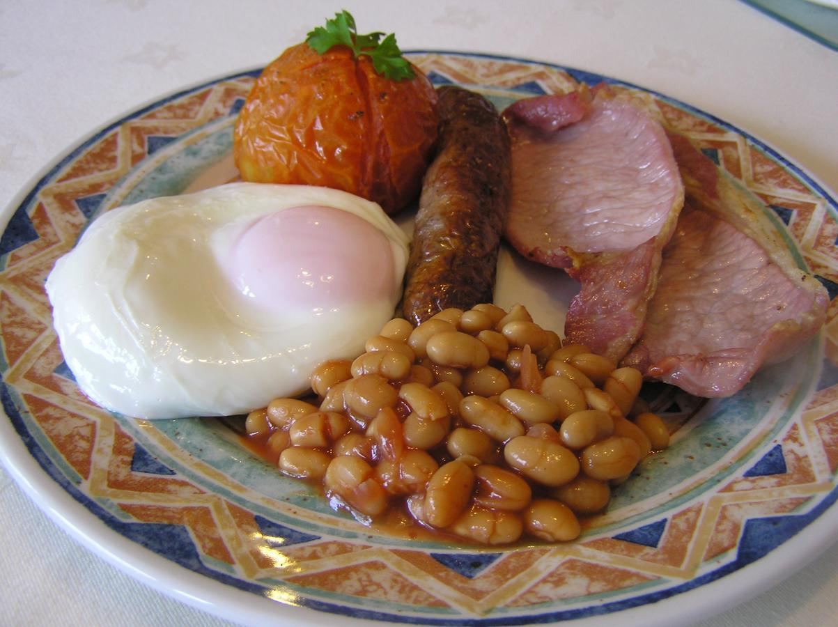 Cooked English breakfast with fried egg, beans, sausage, bacon and tomato