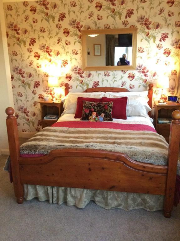 Double room at Kays Cottage with wooden bed, floral wallpaper and red cushions